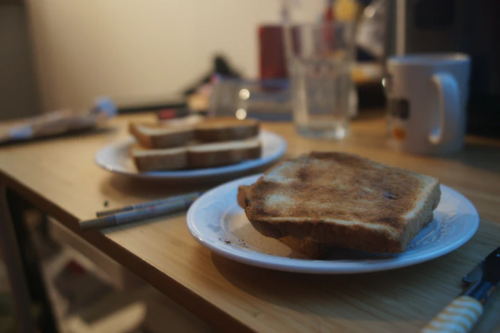 Deux tranches de pain grillé dans une assiette sur une table de cuisine, avec une tasse et un stylo à côté.