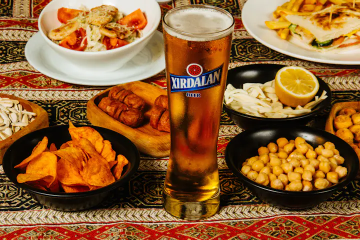 A glass of beer beside plates of food on a wooden table.