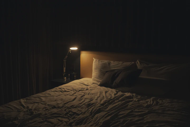 A table lamp glowing softly beside a bed at night.