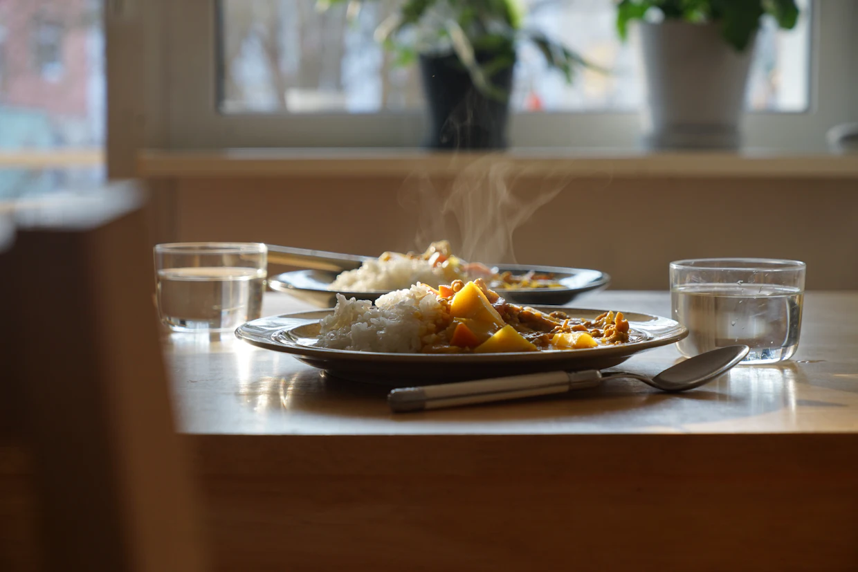 Une assiette de cuisine maison encore fumante, sur une table de cuisine près d'une fenêtre.