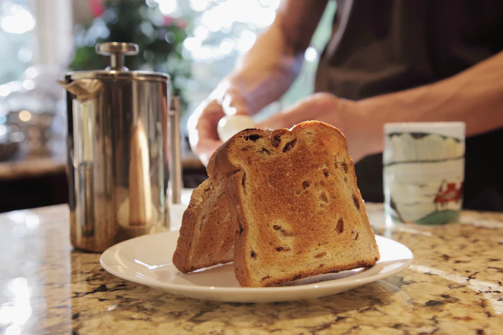 Du pain grillé dans une assiette et une cafetière à piston sur un comptoir, une main qui va prendre la tasse.