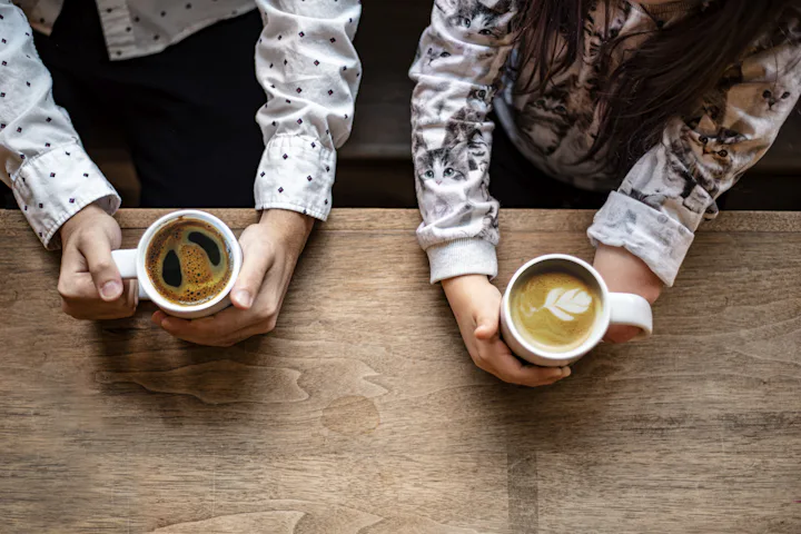 Les mains de deux personnes qui tiennent une tasse, de chaque côté d'une table en bois.