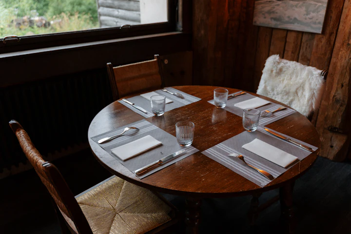 Une table de restaurant ronde en bois dressée pour quatre, avec verres et serviettes pliées.