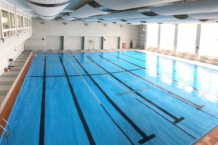 Une piscine intérieure déserte, ses lignes de couloir au fond et l'eau immobile.