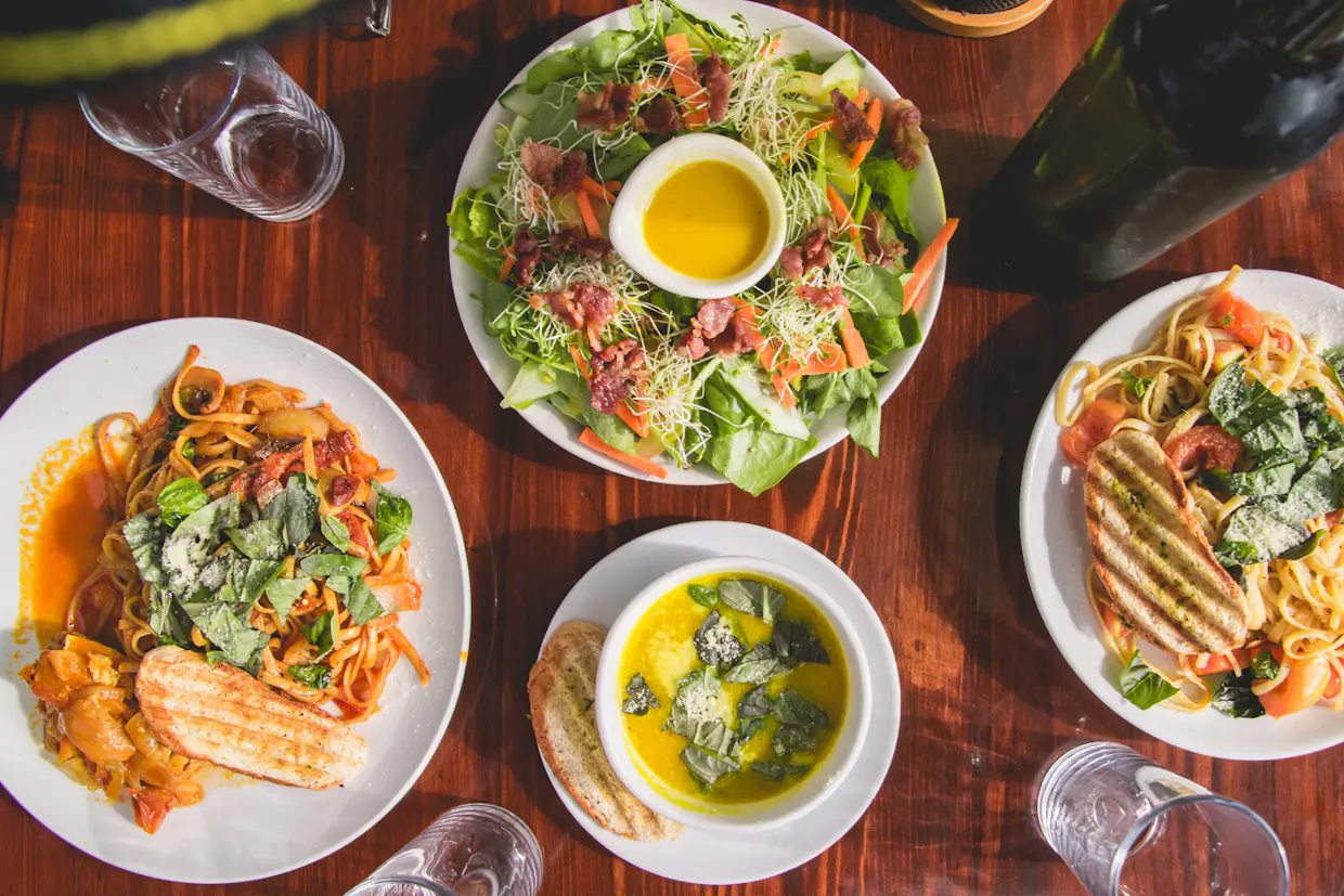 An overhead view of a wooden dinner table with a shared salad bowl in the middle and plates of food around it.