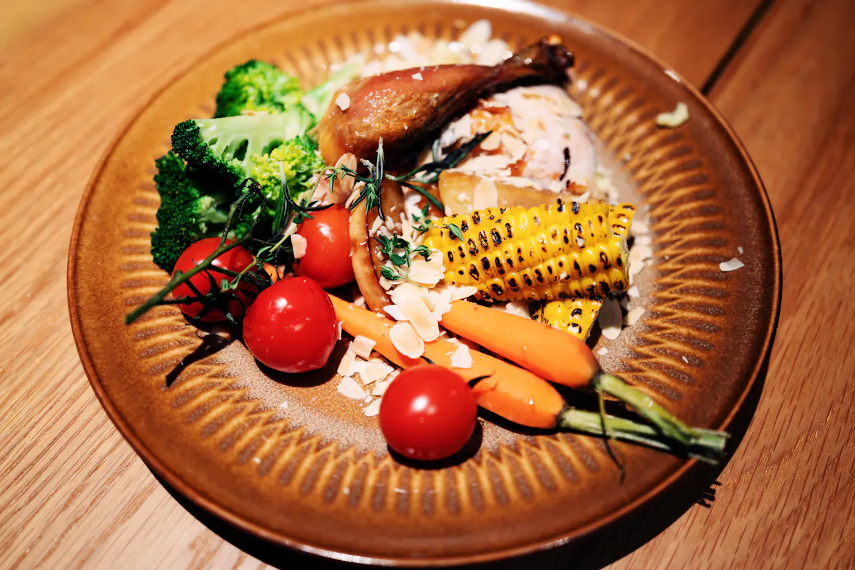 Une assiette de poulet rôti avec du riz, du brocoli, des carottes, du maïs et des tomates sur une table de bois.