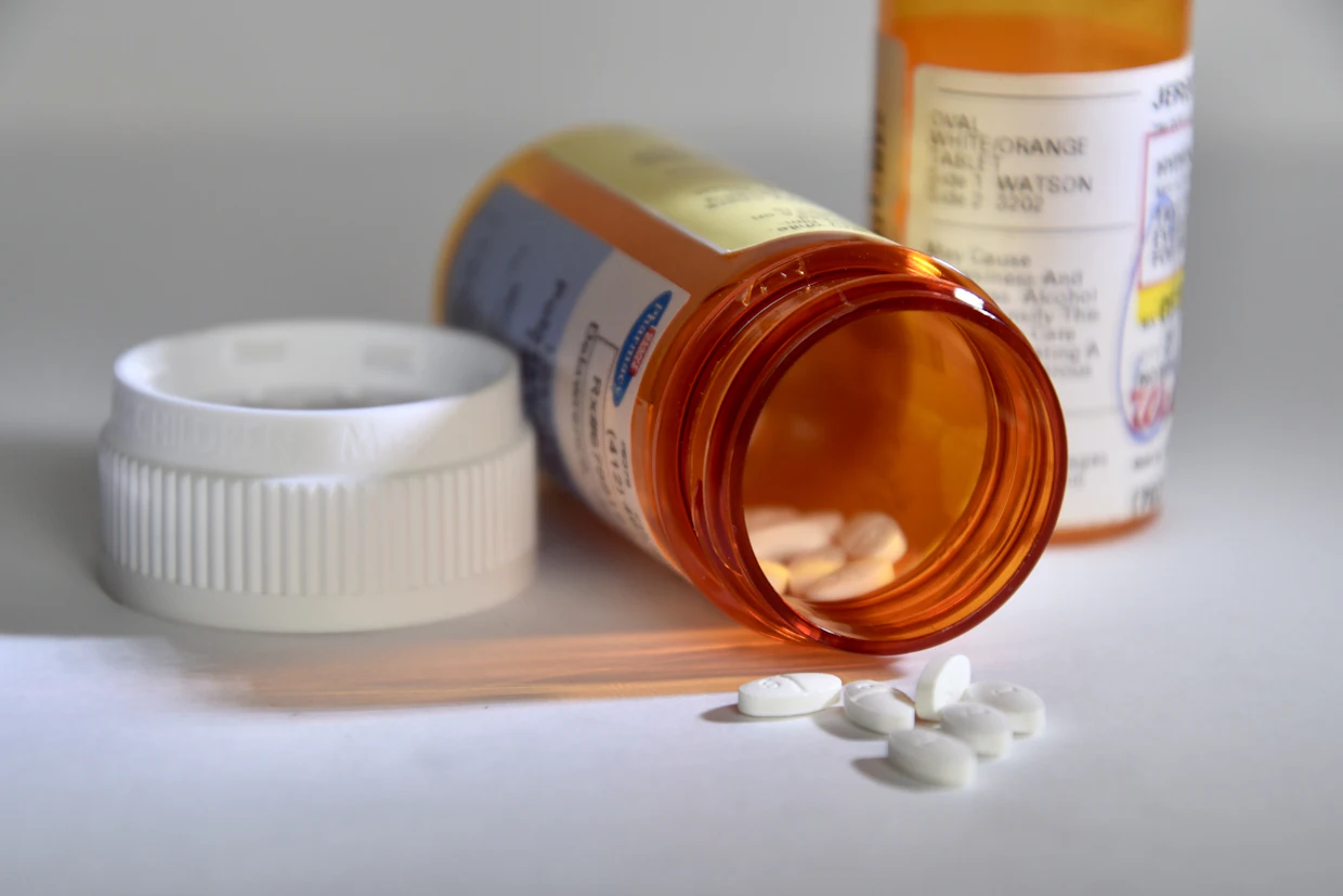 Deux flacons de médicaments sur une surface blanche, dont un couché avec des comprimés qui en sortent.
