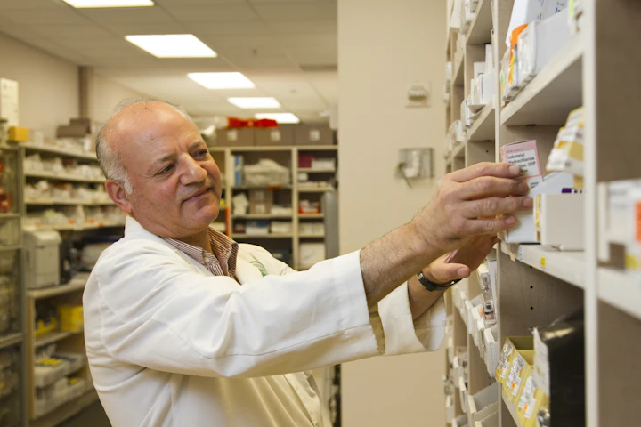 Un pharmacien qui prend une boîte sur les tablettes derrière le comptoir.