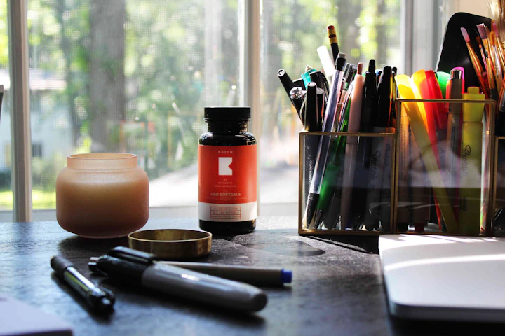 Un flacon de comprimés à côté d'un pot à crayons et d'un carnet, sur une table près d'une fenêtre.