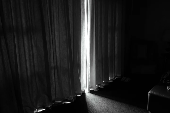A dark room with drawn curtains and a thin line of daylight showing at the gap.