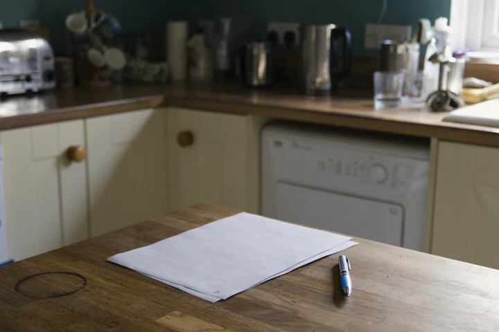Blank sheets of paper and a pen on a wooden kitchen counter.