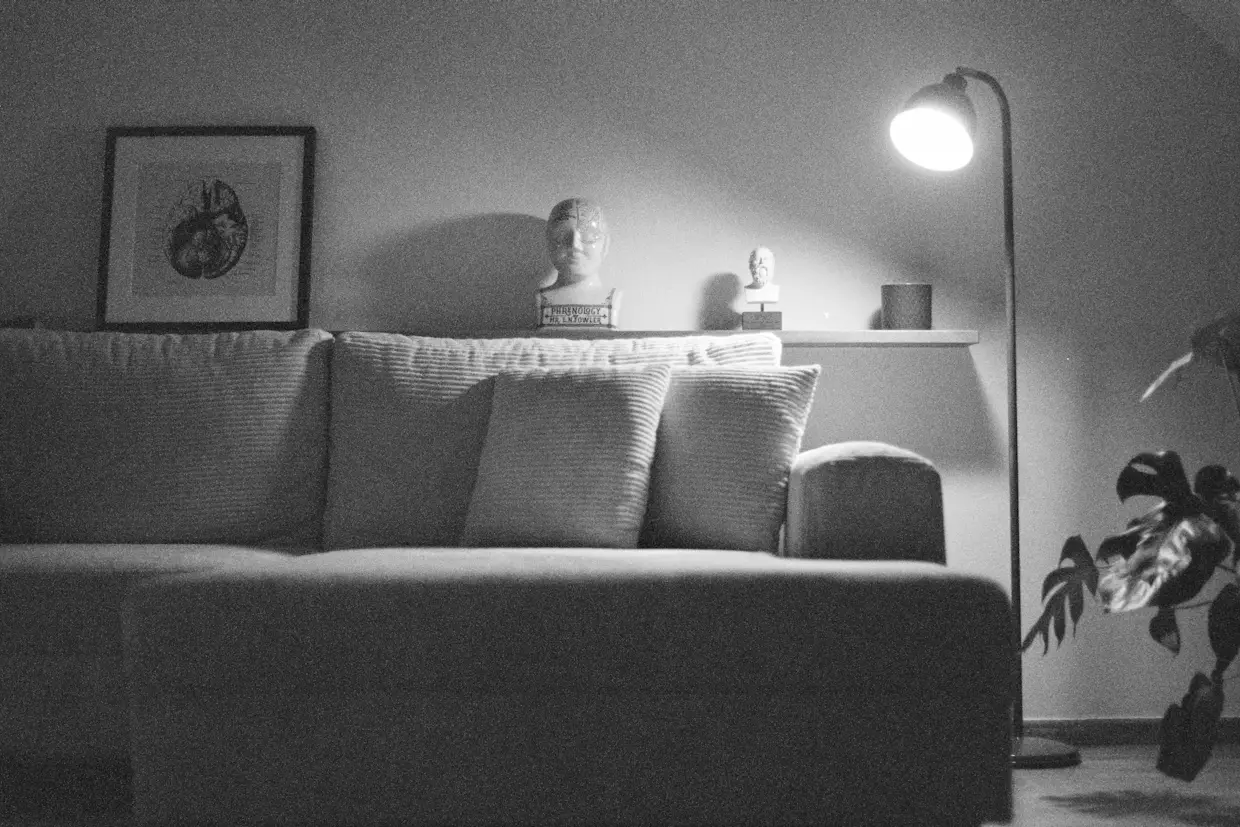 A quiet living room in the evening with a single floor lamp lit beside an empty couch.
