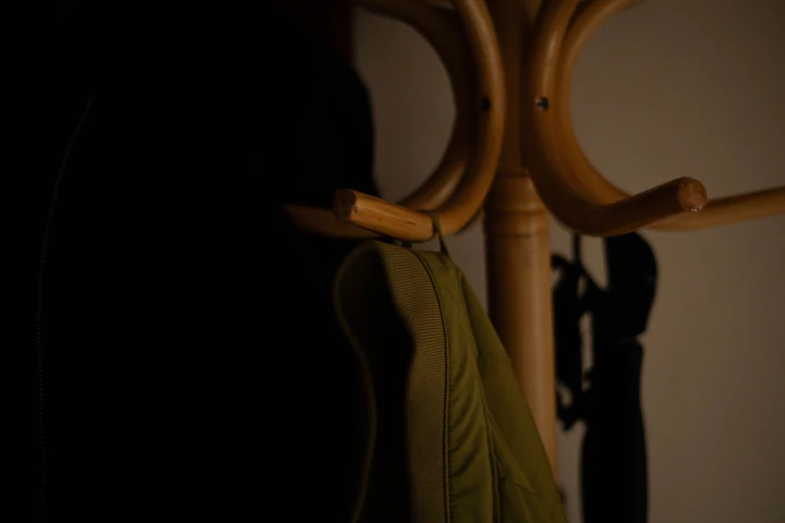 A coat and a bag hung on a wooden coat rack in a dimly lit hallway at the end of the day.