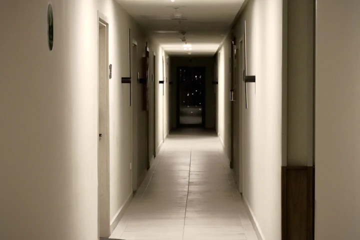 Un long corridor d'immeuble en soirée, avec des portes de chaque côté.