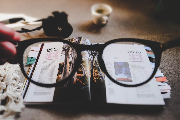 Une paire de lunettes posée sur un magazine ouvert, avec une tasse par terre derrière.