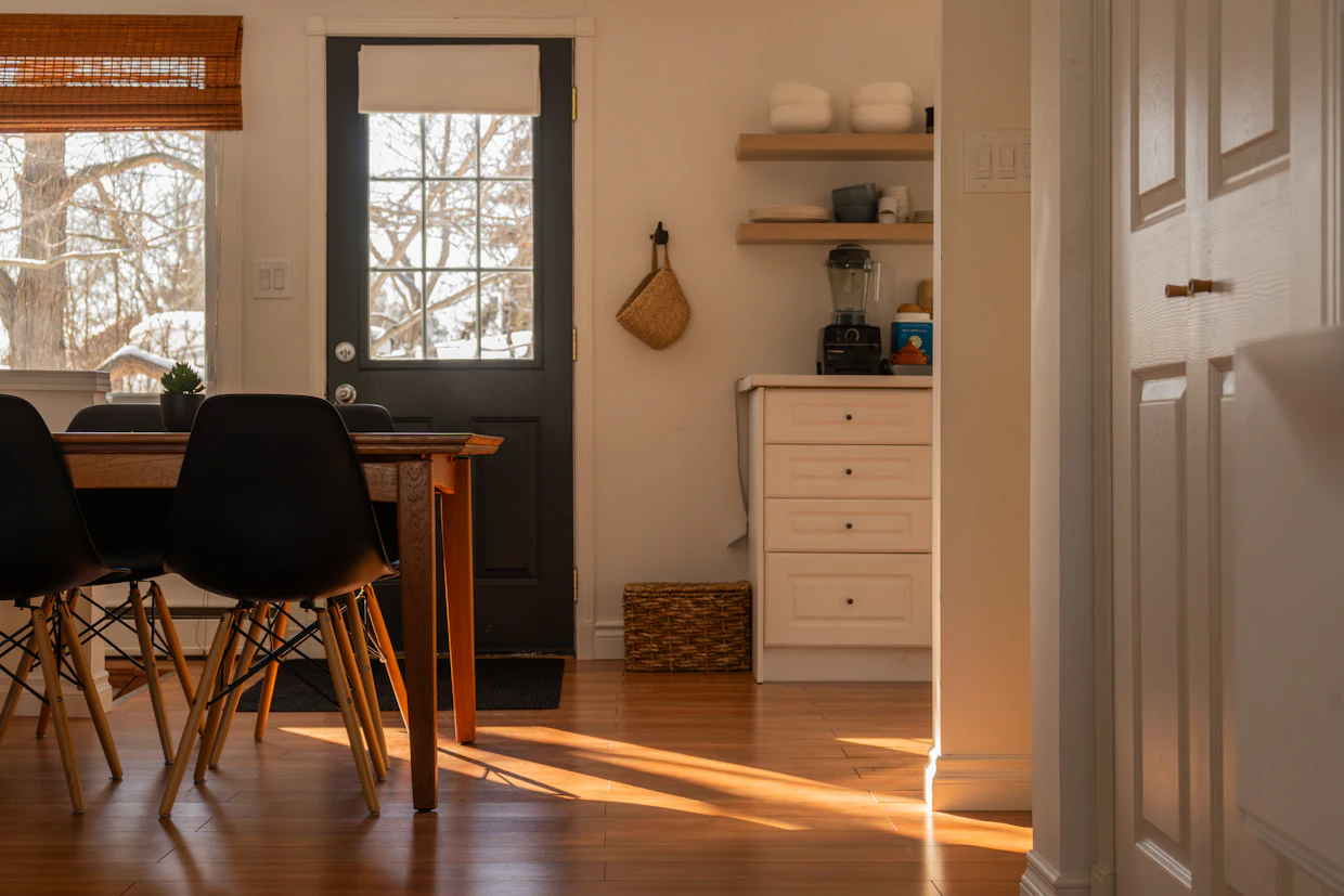Une table à manger et des chaises près d'une porte arrière, avec le soleil bas sur le plancher de bois.