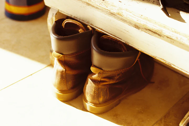 Une paire de bottes de cuir usées rangées sous un banc dans la lumière chaude de l'après-midi.