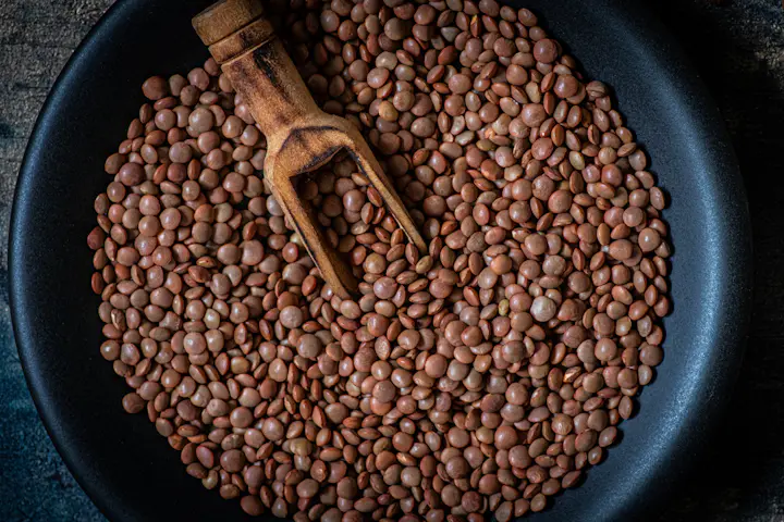 A pan of red lentils with a wooden scoop resting in them.