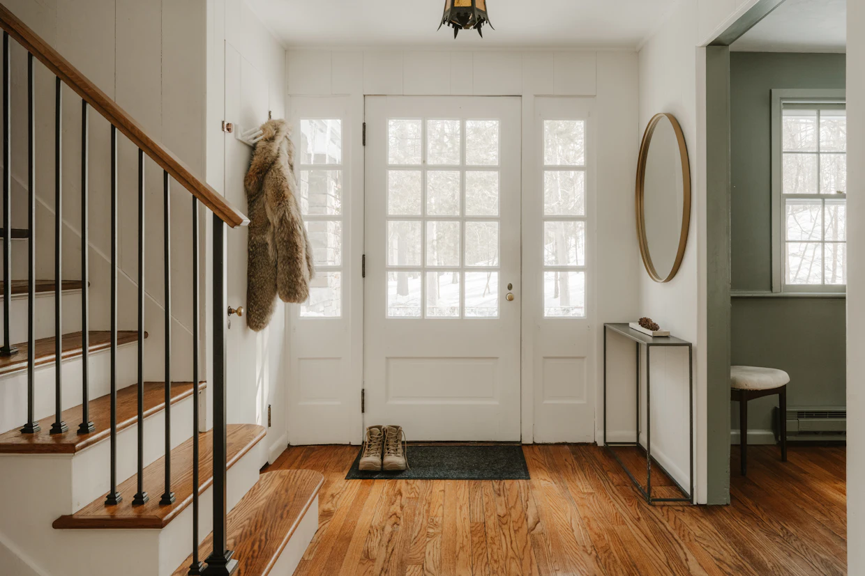 Une entrée avec un plancher de bois, un tapis et des souliers près de la porte.