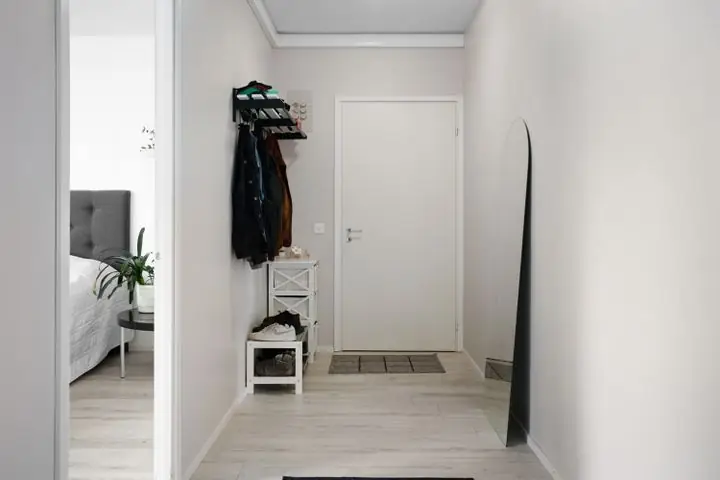 Un corridor clair dans une maison, avec un portemanteau et des souliers rangés près de la porte.