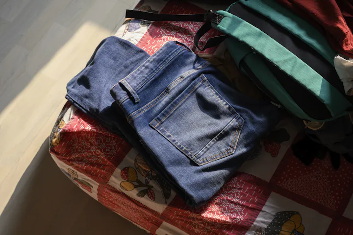 A pair of jeans lying on a made bed.