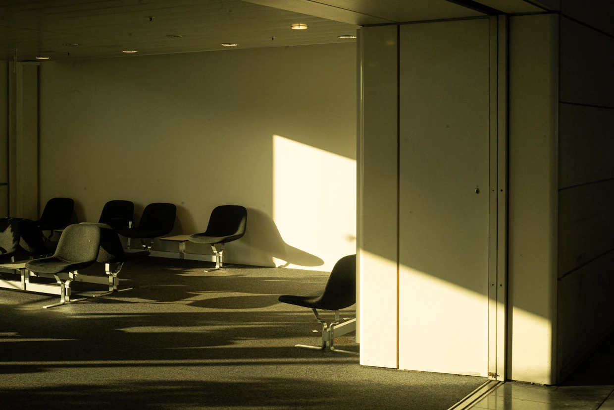 Une rangée de chaises vides dans une salle d'attente, la lumière du jour tombant sur le plancher.