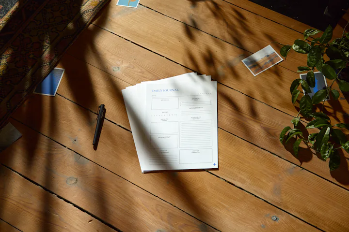 Une feuille imprimée et un stylo sur un plancher de bois, dans la lumière du jour et l'ombre des feuilles.