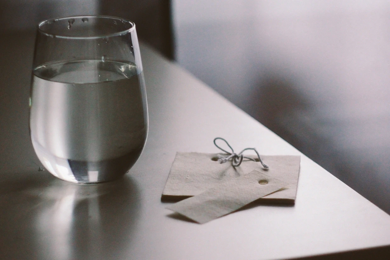 Un verre d'eau sur une table claire à côté de deux petites étiquettes de papier.