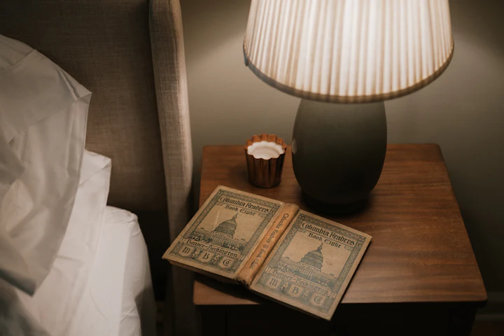 An open book on a bedside table lit by a small lamp at night.
