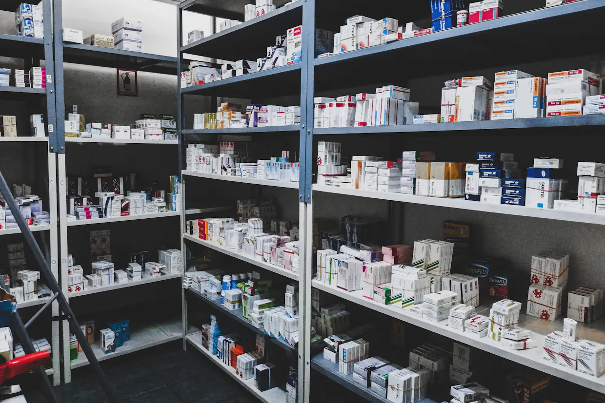 Rows of pharmacy shelves stocked with boxes of medication, nobody in the frame.