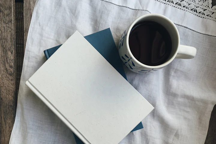 Un carnet fermé et une tasse de café noir sur un linge posé sur une table de bois.