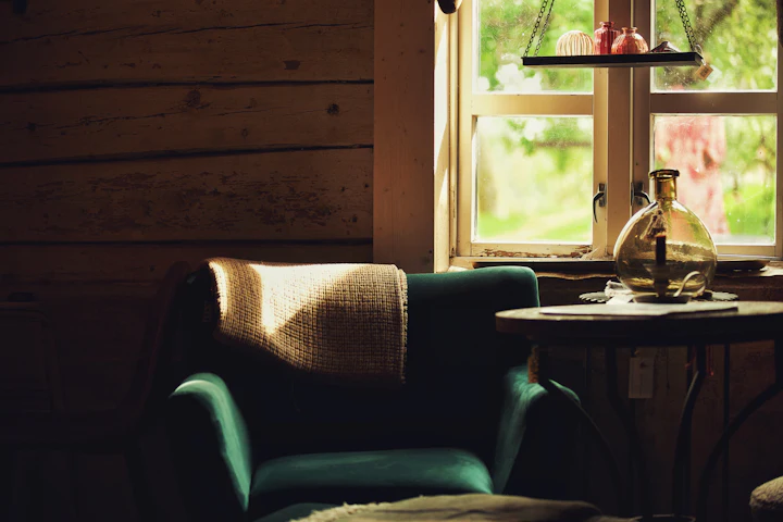 Un fauteuil à côté d'une petite table devant une fenêtre ensoleillée, sans personne dans la pièce.