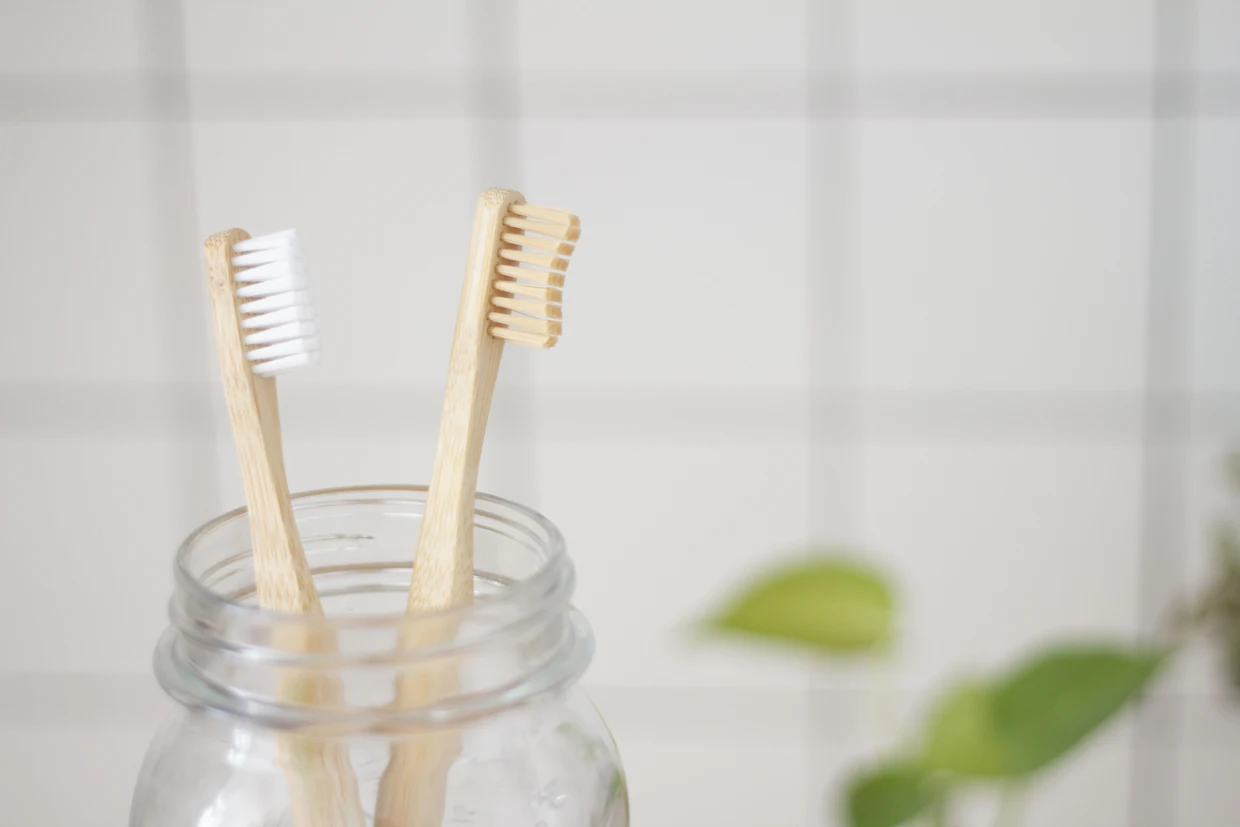 Deux brosses à dents en bois dans un pot de verre devant un mur de salle de bain carrelé.