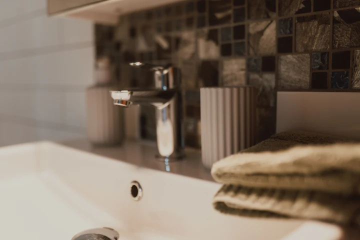 Un lavabo de salle de bain avec un verre à côté du robinet et une serviette pliée sur le comptoir, en lumière chaude du jour.